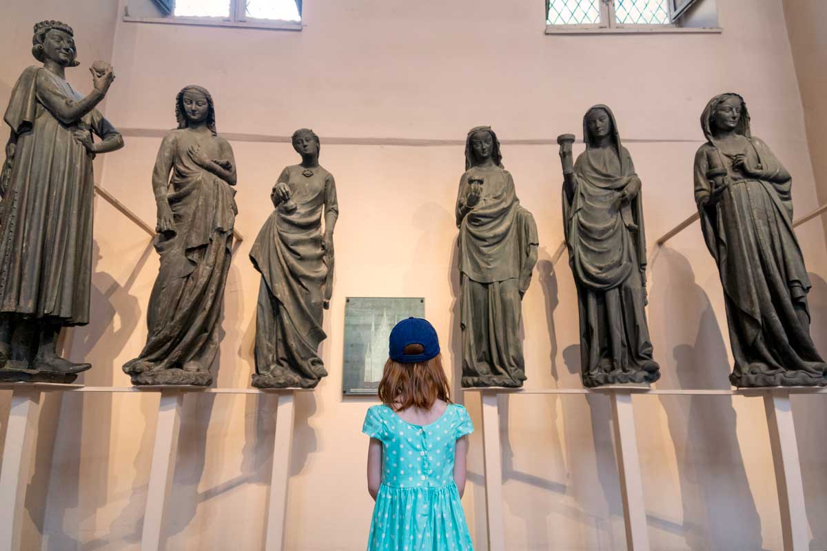 kid in a museum in front of six statues